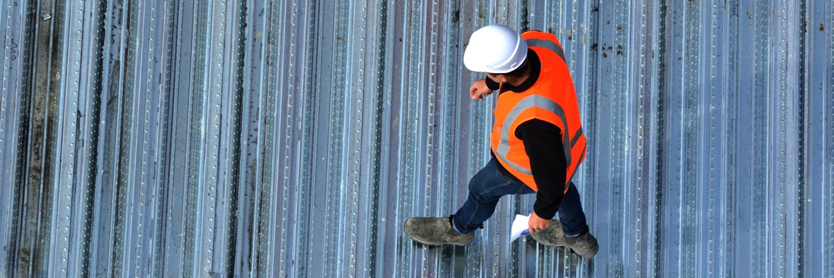 A worker in an orange vest performs a roof inspection as part of the Garland building evaluation process.