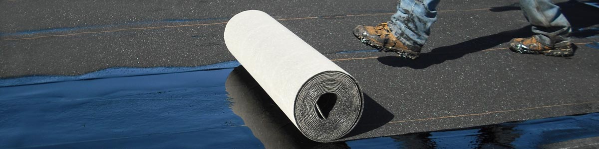 A worker unrolls base sheet roofing with his boot.